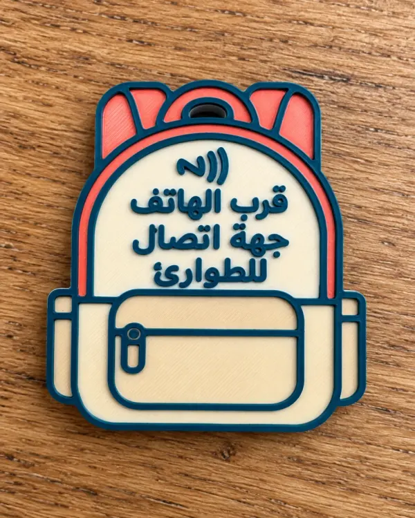 بطاقة NFC بشكل شنطة مدرسية مطبوعة ثلاثية الأبعاد، مكتوب عليها «قرب الهاتف جهة اتصال للطوارئ»